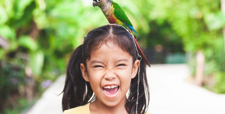 A young girl smiles while a bird sits on her head